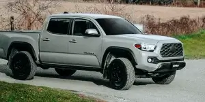 Toyota Tacoma truck with all terrain tires parked on gravel road surrounded by green grass and trees.